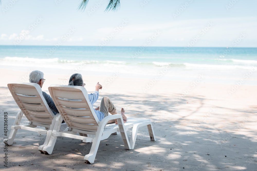 Retired couple resting on a adirondack chair by the beach in the sunlight and clean sandy beach. Retirement Planning Ideas and Happy Life.