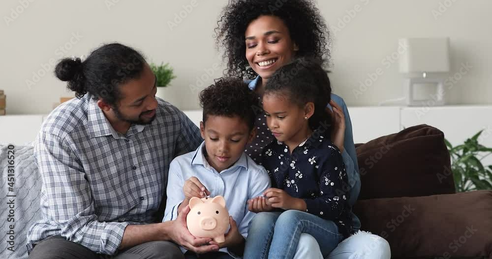 Smiling young african american couple parents holding on knees interested little children, teaching financial literacy at home. Curious small kids sibling learning saving money or budget management. Smiling young african american couple parents holding on knees interested little children, teaching financial literacy at home. Curious small kids sibling learning saving money or budget management.