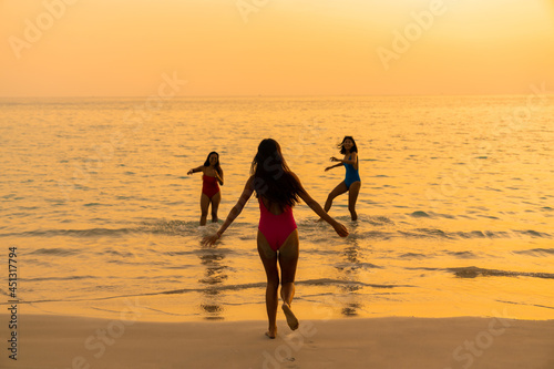 Asian woman friendship in colorful swimwear walking and playing sea water together on the beach at summer sunset. Female girl friends enjoy and having fun outdoor activity lifestyle on summer vacation