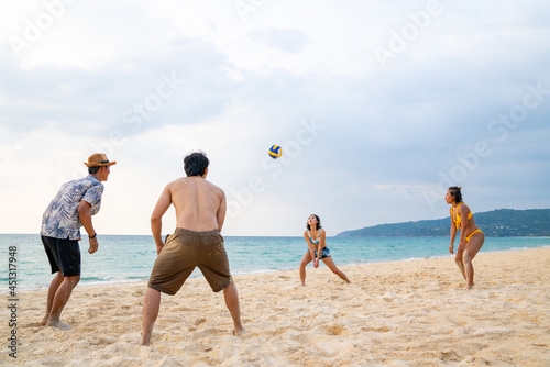 Group of Asian man and woman friends playing beach volleyball together on tropical beach in sunny day. Male and female friendship enjoy and having fun outdoor lifestyle activity on summer vacation
