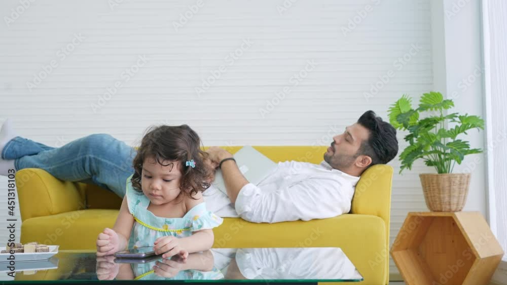 4K Hispanic father lying on sofa and working on digital tablet while little child girl daughter playing game on smartphone in living room. Happy family enjoy indoor activity with technology together. 4K Hispanic father lying on sofa and working on digital tablet while little child girl daughter playing game on smartphone in living room. Happy family enjoy indoor activity with technology together.