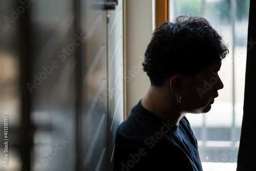 Depressed Asian man sitting by the window in bedroom with stressed and hopeless face. Loneliness sad man being alone in bedroom thoughtful with negative emotion. Mental health and life problem concept