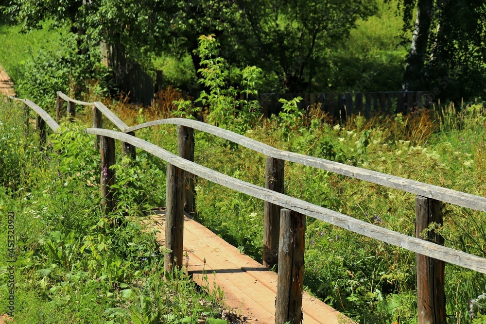Old wooden footbridge with handrails across a small stream 