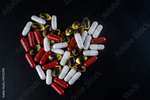 Different pills and capsules arranged in a heart like shape, isolated on a black background, macro photo