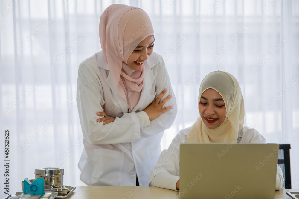 Portrait of young female Asian Muslim doctors are working and discussing with each other while using laptops at the hospital office room Portrait of young female Asian Muslim doctors are working and discussing with each other while using laptops at the hospital office room