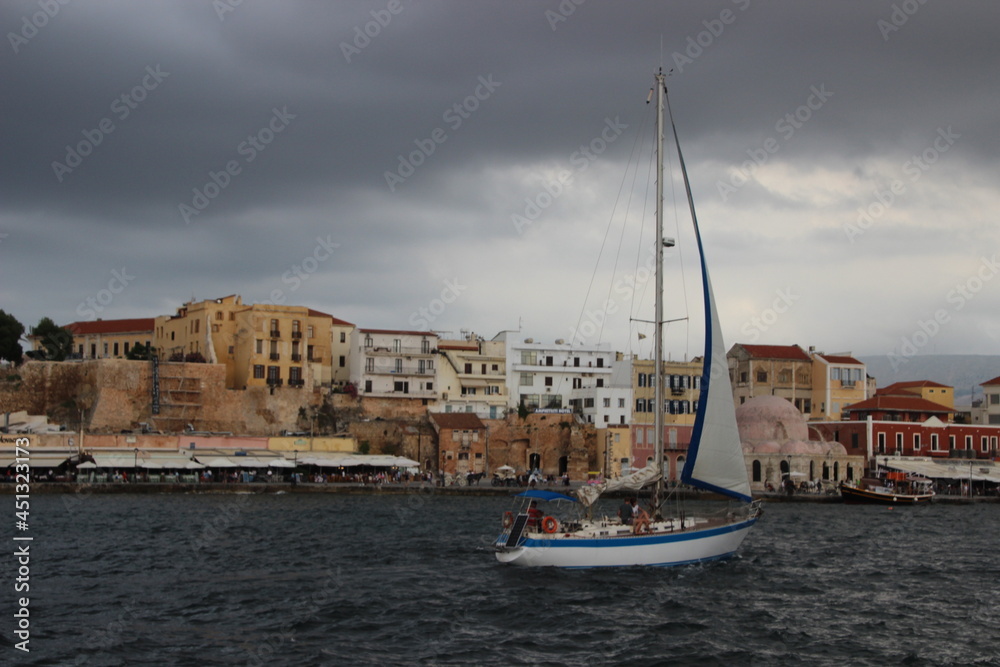 At the Sea, Rauer Tag an der See im Hafen Chania, Kreta, Griechenland, Wolken ziehen auf, im Vordergrund fährt ein Segelschiff