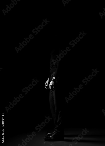 Black and white. Unrecognizable man in black trousers, sweater and shoes standing sideways over dark background. Lower body