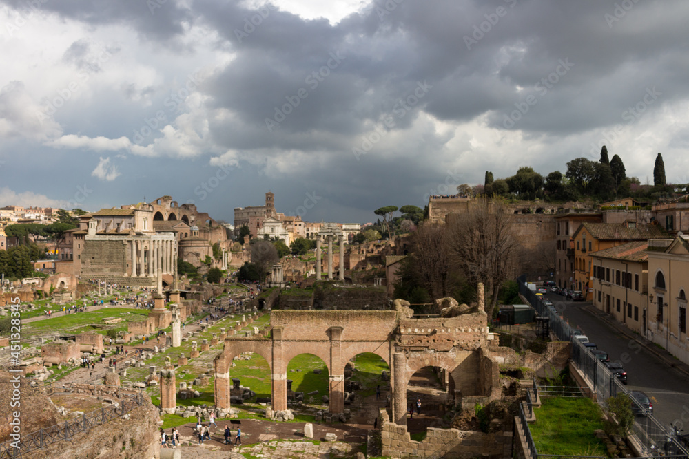 Top view of the Roman forum, illuminated by the sun, against a dramatic sky. Ancient architecture and the urban landscape of historical Rome