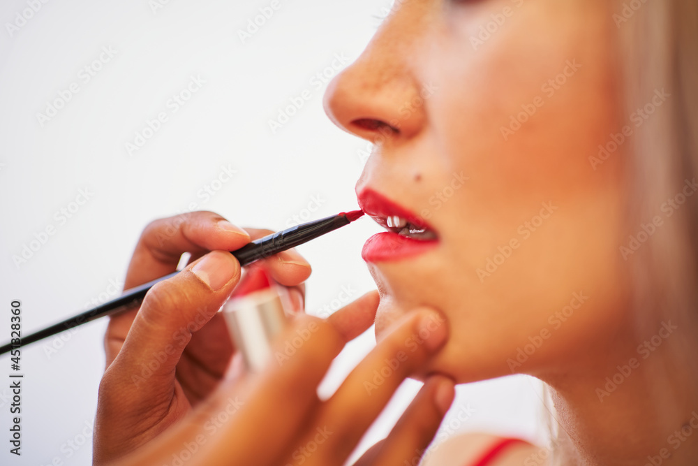 Detail of unrecognizable makeup artist working on a young woman's lips. Beauty concept