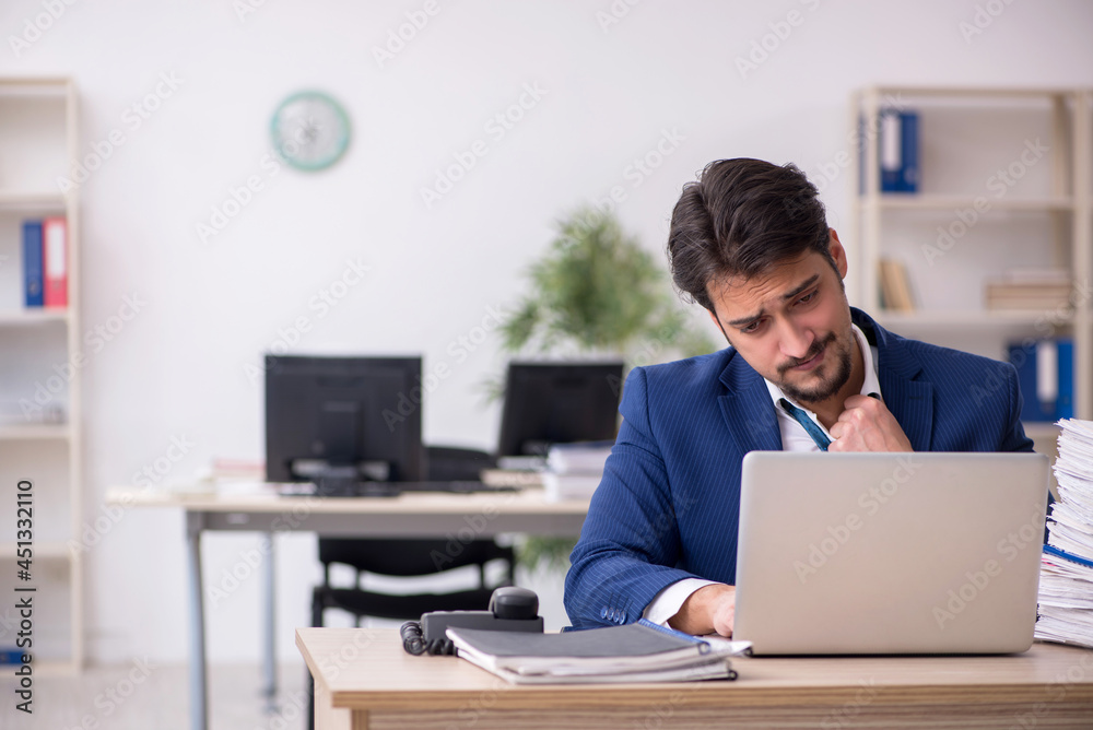 Young male employee unhappy with excessive work in the office Young male employee unhappy with excessive work in the office