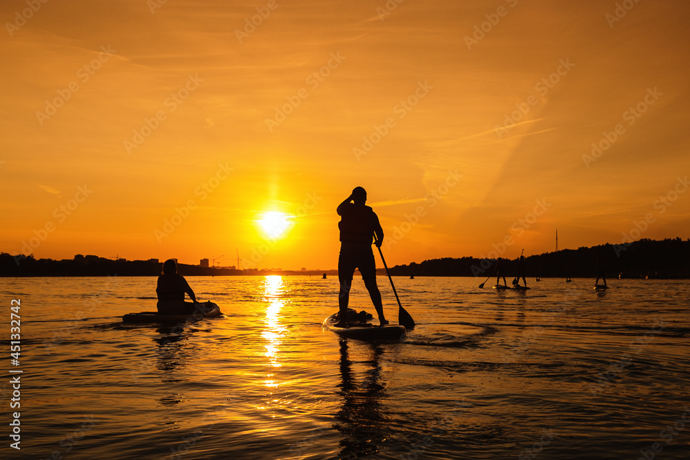 Silhouette of person standing up on sapboard on city river at sunset. Small local travel with family or friends,