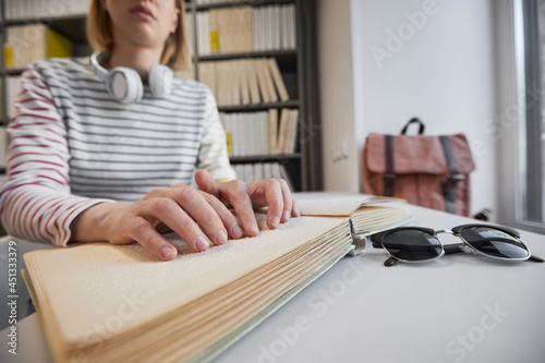 Close up of young blind woman reading Braille book in college library, copy space