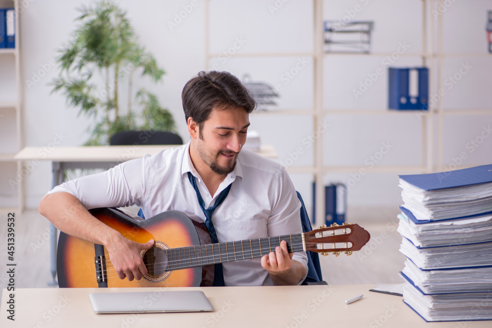 Young male employee playing guitar at workplace Young male employee playing guitar at workplace