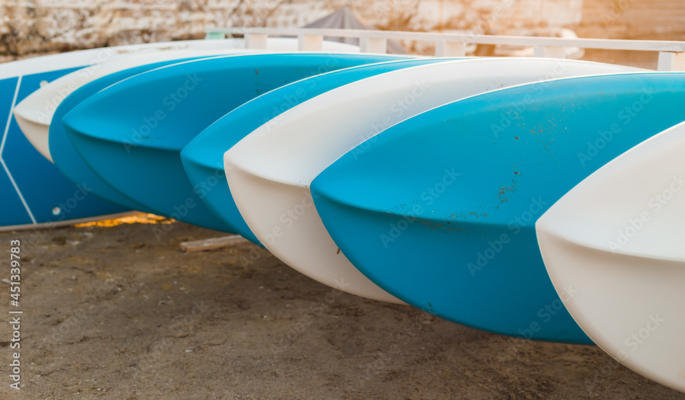 Many different sup boards on the beach. Surfing and SUP boarding equipment in sunset lights close-up. Outdoor water sports. Surfing lifestyle concept. Many different sup boards on the beach. Surfing and SUP boarding equipment in sunset lights close-up. Outdoor water sports. Surfing lifestyle concept.