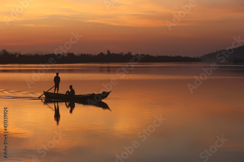 One man standing and paddling boat and other man sitting on wooden boat at beautiful dusk on river Sangu in Bandarban, Bangladesh .