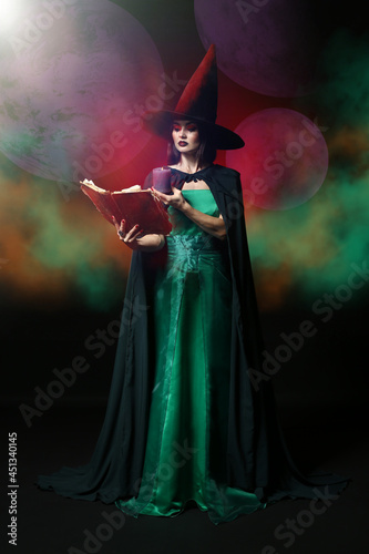 Young witch with spell book and candle on dark background