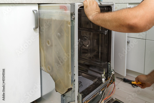 fixing a home dishwasher. the master pulls out the built-in dishwasher for repair