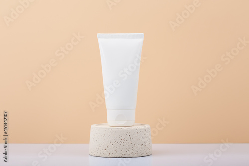 White plastic cosmetic tube with cream, balm, mask, scrub or lotion on pink pedestal against pink background with copy space. Concept of natural organic skin care products for manicure, hands or face