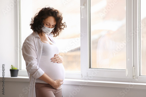Young pregnant woman in medical mask near window at home Free Download Young pregnant woman in medical mask near window at home - GFXLoad
