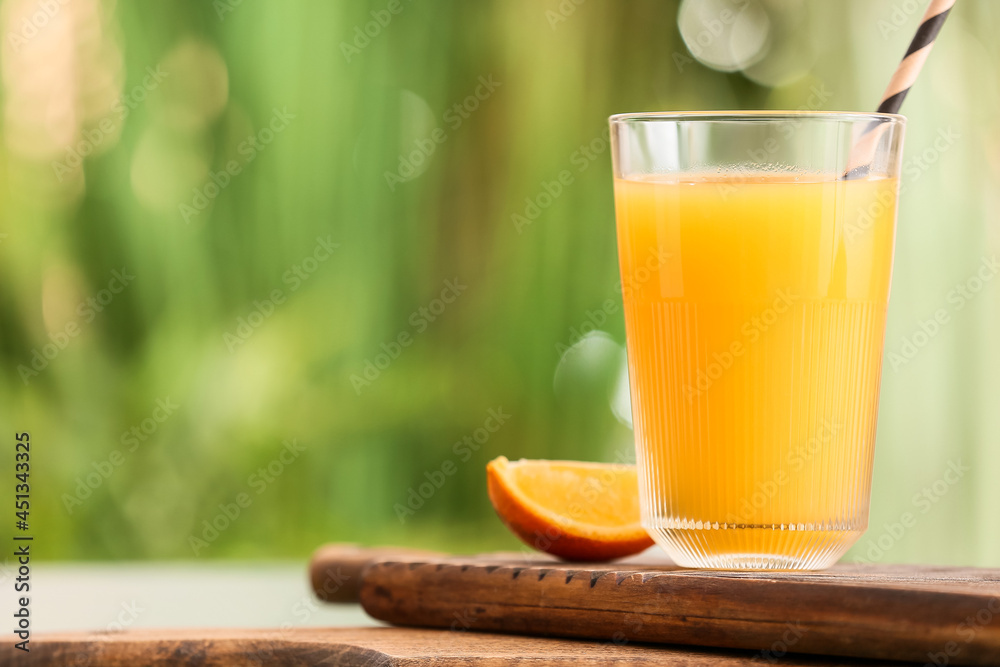 Fototapeta premium Board with glass of tasty orange juice on table outdoors