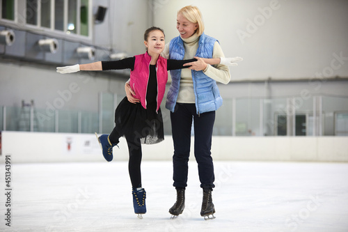 Fotografie, Obraz Full length portrait of Asian girl figure skating on rink with female coach help