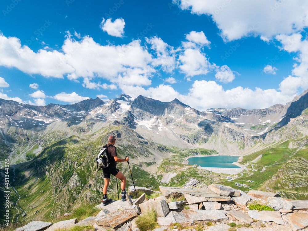 Hiker looking at view of idyllic blue alpine lake high up on the mountains, scenic landscape rocky terrain at high altitude on the Alps, panoramic view