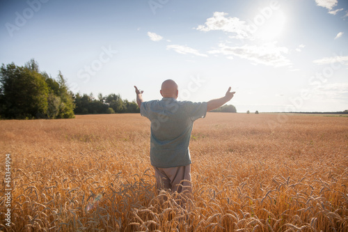 Mature man standing back in wheat field at sunset