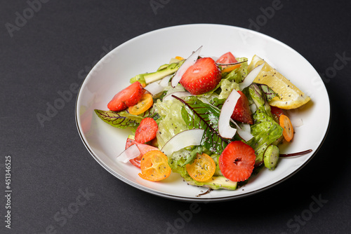 Spinach salad with strawberries, cherry tomatoes and coconut chip slices in a white plate over black background.