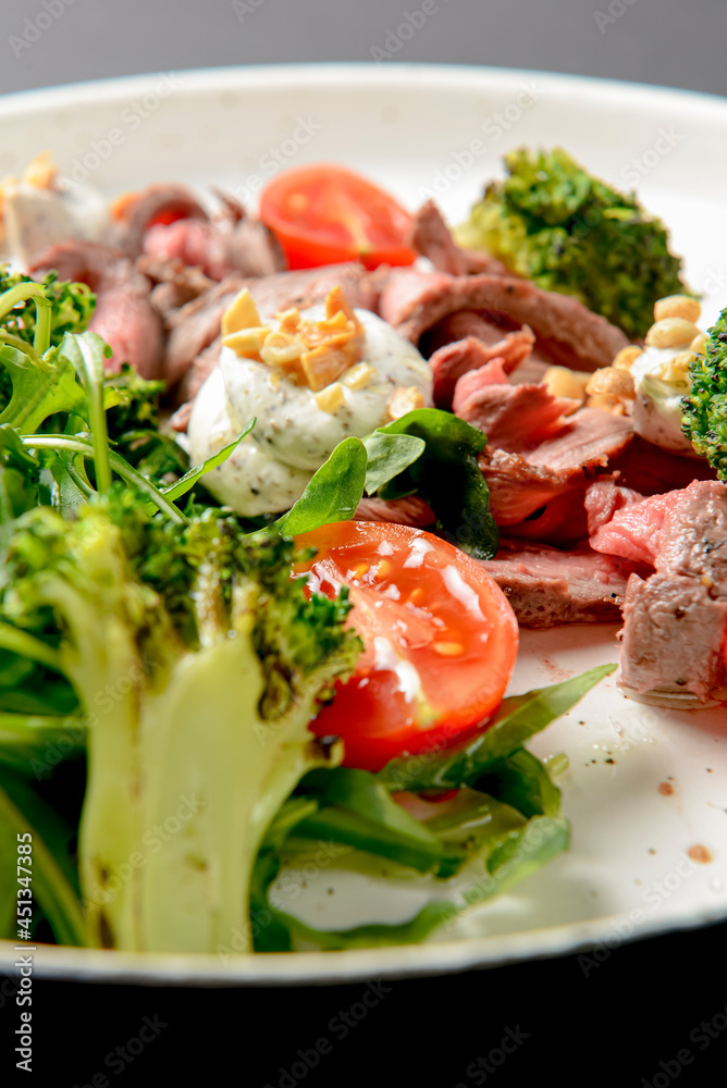 Healthy salad made from meat, cherry tomatoes, broccoli, goat cheese and fresh arugula served in a white plate. Healthy salad made from meat, cherry tomatoes, broccoli, goat cheese and fresh arugula served in a white plate.