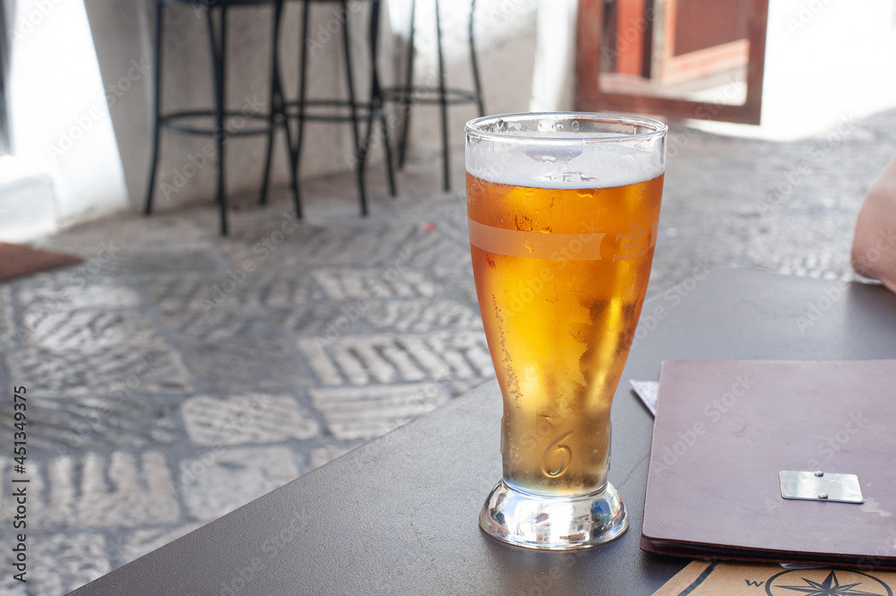 cold refreshing beer in a misted glass on a table in a cafe on a stone-paved street
