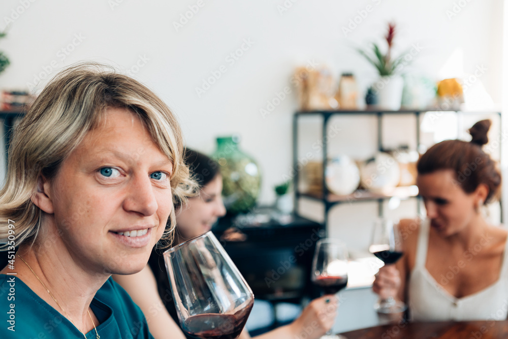 Mature woman looking at camera while drinking wine and enjoying time with friends at bar restaurant - Focus on left face