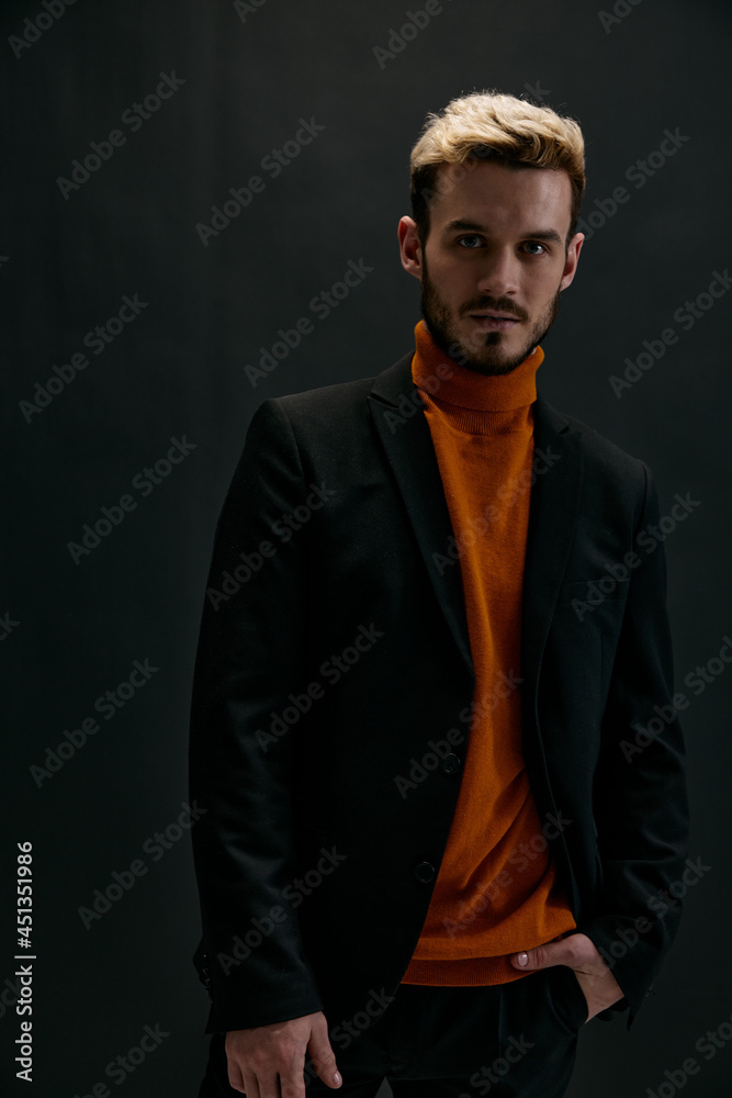 blond man in a coat and an orange sweater on a dark background front view model