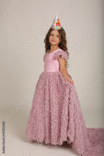 beautiful happy brown-haired girl with curly hair in a pink dress dancing birthday