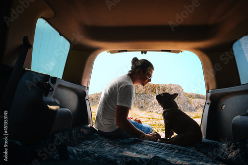 Man and french bulldog sitting in car trunk against mountain © adrianad