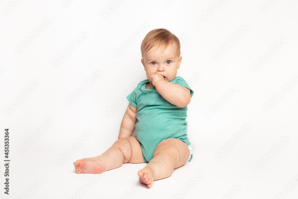 cute Caucasian one year old baby sucks thumb and scratches his first teeth. toddler boy teasing on white background in studio. baby care and child health concept cute Caucasian one year old baby sucks thumb and scratches his first teeth. toddler boy teasing on white background in studio. baby care and child health concept
