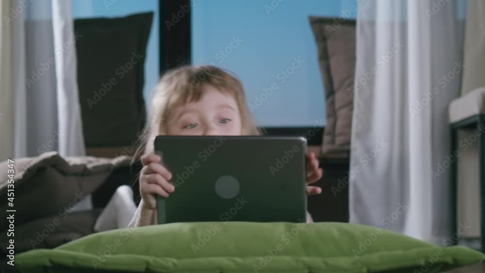 Adorable Kid Girl Using Digital Tablet Watching Cartoons Lying on Bed at Home. Close up Portrait of Cute Child Playing Game on Tablet PC Relaxing on Sofa Adorable Kid Girl Using Digital Tablet Watching Cartoons Lying on Bed at Home. Close up Portrait of Cute Child Playing Game on Tablet PC Relaxing on Sofa