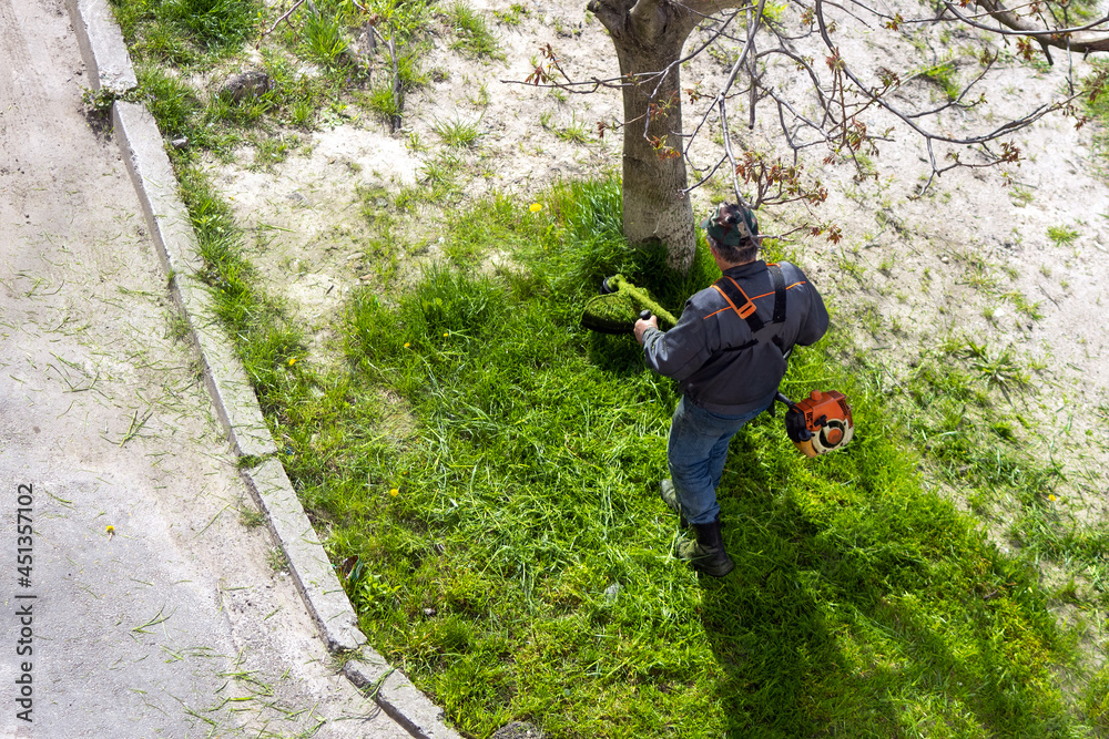 Obraz premium The gardener cuts the grass with a hand-held electric lawn mower.