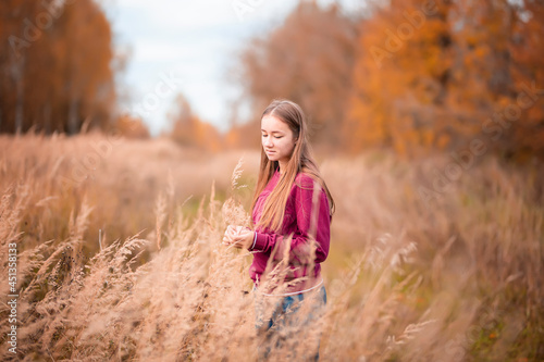 girl stand on background grass in outdoor, in field in sunlight. half length, upper half. the wind blows hair. Autumn day.