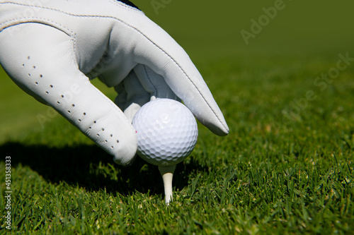 Close up golf ball on green grass field. Golf club. Hand putting golf ball on tee in course. Golf ball on tee ready to be shot.