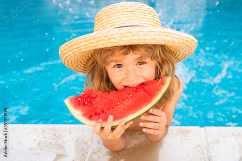 Kid eats watermelon in the pool. Cute boy eating slice of red watermelon on the beach, happy caucasian boy watermelon against the blue water.