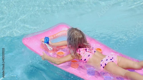 Blonde girl swims in the pool on an inflatable mattress