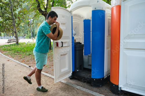 Man covering his nose while is opening the door of a smelly portable toilet. photo