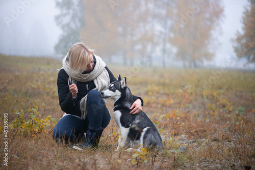 Young woman with beautiful siberian husky dog playing in city park during autumn