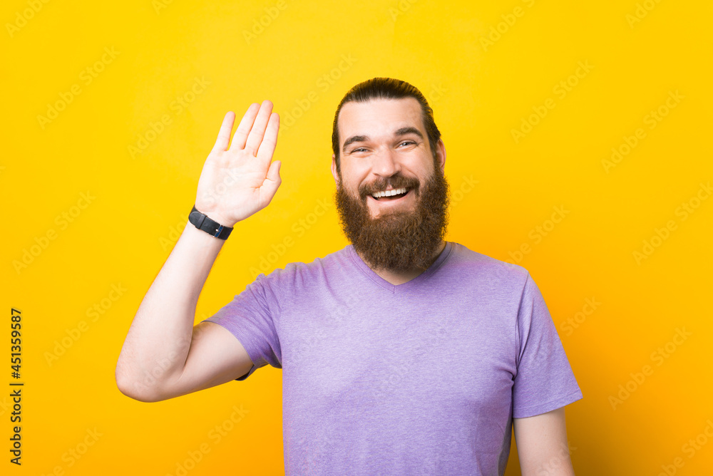 Photo of happy smiling bearded man waving hand over yellow background Photo of happy smiling bearded man waving hand over yellow background