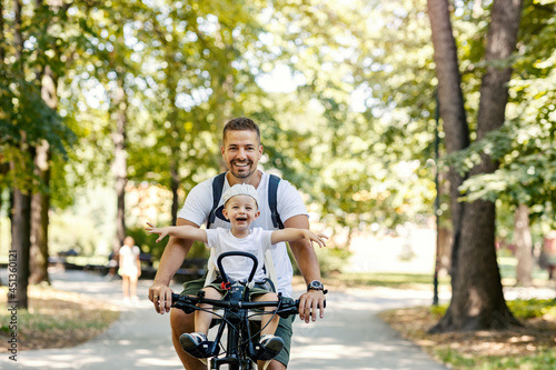 Father and son ride bicycles. Toddlers sit in a basket of bikes and wander around. Summer sunny family day, family bonding time. Active family weekend, vacation in the park with the family © dusanpetkovic1