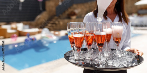 Midsection of waiter offering champagne at poolside.Serving with ice on a tray. Swimming pool party concept. photo