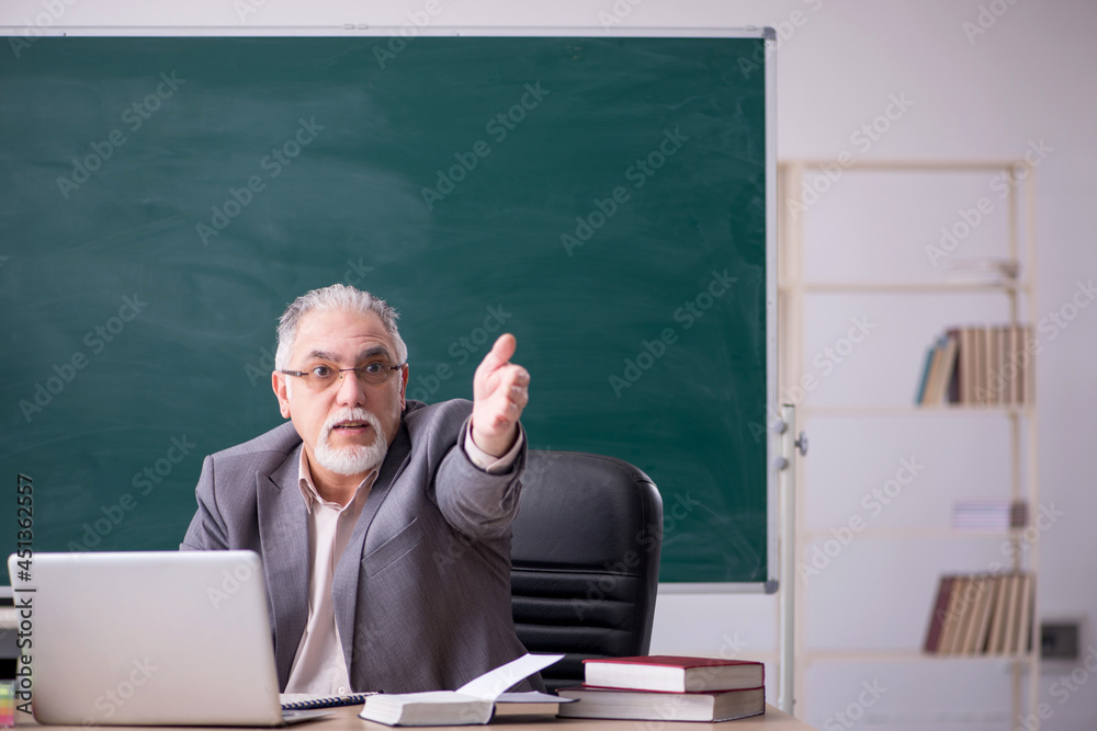 Old male teacher in front of blackboard Old male teacher in front of blackboard