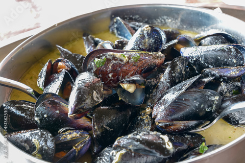 close up of cooked mussels in a stainless steel pot with spoon