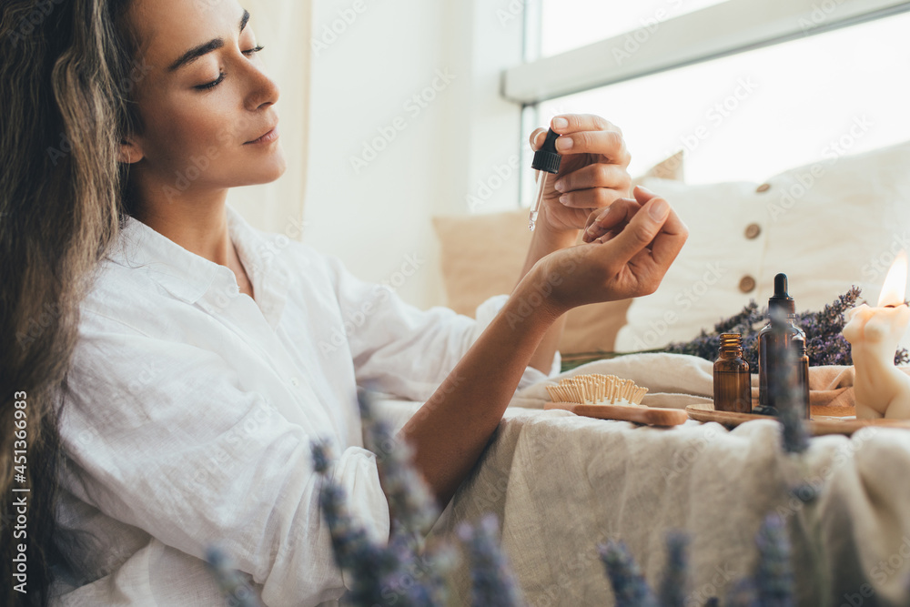 Young woman applying natural organic essential oil on hair and skin. Home spa and beauty rituals. - obrazy, fototapety, plakaty 
