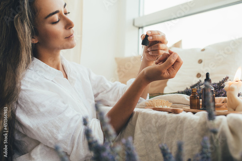 Young woman applying natural organic essential oil on hair and skin. Home spa and beauty rituals. photo